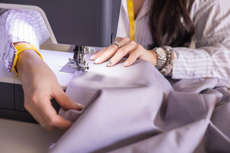 Woman plus size fashion designer uses a sewing machine in her studio.