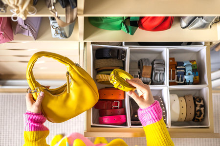 A young woman matches a belt to a fashionable yellow bag at home. Storage of belts, bagsの写真素材