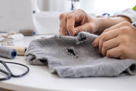 A woman uses her hands to sew up a hole in a gray knitted garment with a needle and thread.の写真素材