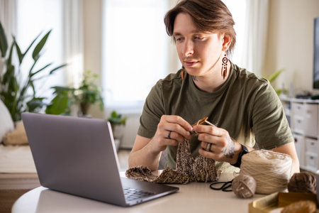 Feminine hipster man crochet handmade use hook knitting needles and wool yarn relaxing on couch.の写真素材