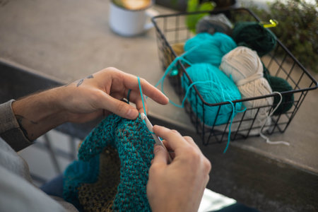 Male hands crochet handmade artwork use wool yarn and hook over table with coffee top viewの写真素材