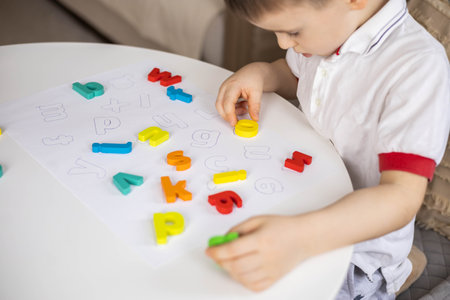 A Caucasian light-haired boy of five years old with blue eyes is putting together a puzzleの写真素材