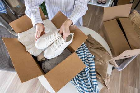 Woman packing clothes and shoes into cardboard box seasonal comfortable storage organize top viewの写真素材