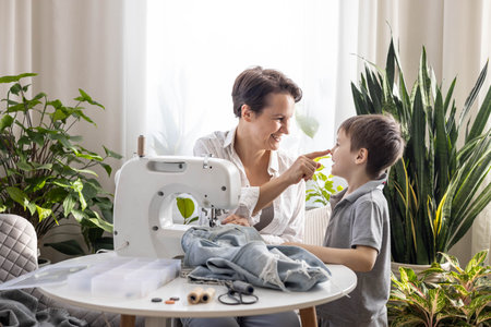 Mom and son are repairing old torn jeans using a sewing machine. A woman teaches a boy to sewの写真素材
