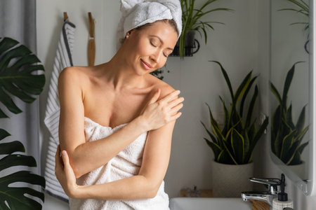 A young beautiful woman in a white terry towel admires herself in front of a mirror in her bathroom.の写真素材