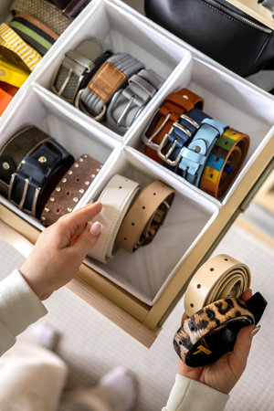 A young beautiful woman puts a convenient order in storing belts in her home wardrobe.