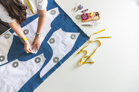 A woman dressmaker lays out pattern details on denim and cuts clothes. Top view.