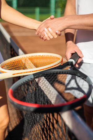 Man and woman tennis player shaking hands through grid playing tournament on sportive court closeupの写真素材