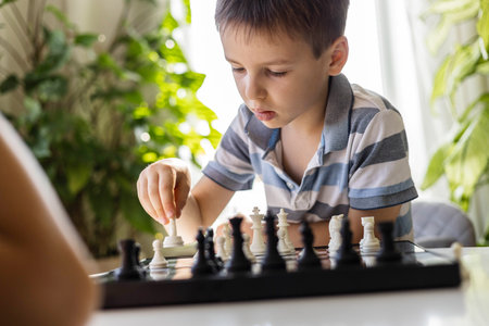 Children play chess at home at a round white table. Boys brothers, siblings spend their free timeの写真素材