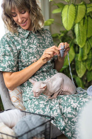 A young girl crochets from gray yarn and strokes a hairless cat.