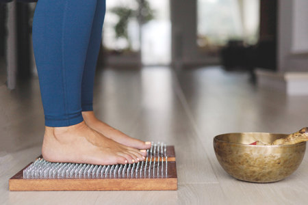 Yoga woman legs standing on nails with singing meditation bowl top view closeupの写真素材