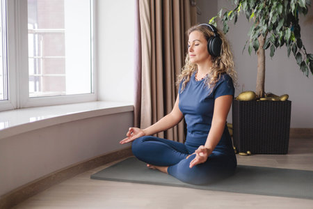 Smiling yoga woman meditation in lotus position listening music use headphones at homeの写真素材