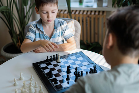 Children brothers play chess at home at a round white table in the living room on a chessboard.の写真素材