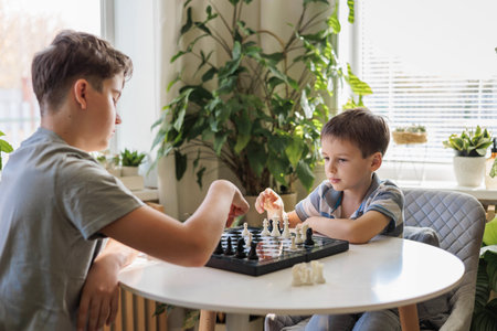 Children brothers play chess at home at a round white table in the living room on a chessboard.の写真素材