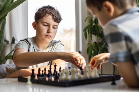 Children play chess at home at a round white table. Boys brothers, siblings spend free time at homeの写真素材