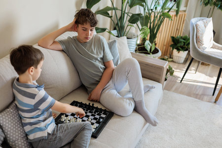 Children brothers play chess on the couch on the chessboard at home.の写真素材