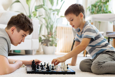 Siblings playing chess on the floor in the living room. Children boys spend their free time at home.の写真素材