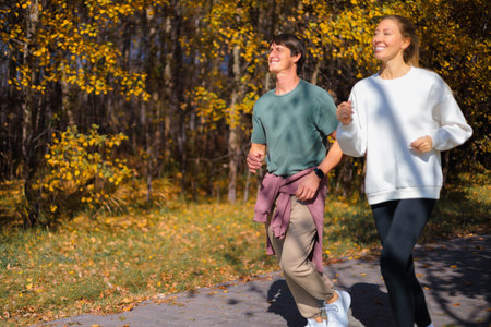 Young beautiful couple jogging in city beautiful autumn park and forest, enjoying outdoor sports.の写真素材