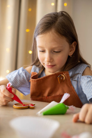 A little girl decorates a Christmas gingerbread mitten with icing. Concept Christmasの写真素材