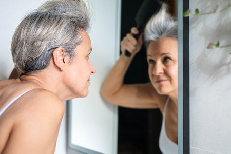 European beautiful and smiling middle-aged woman combing her gray hairの写真素材