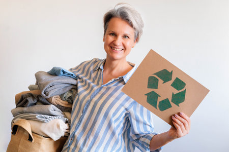Gray haired woman with pile of clothes and recycling reusing signboard isolated on white backgroundの写真素材
