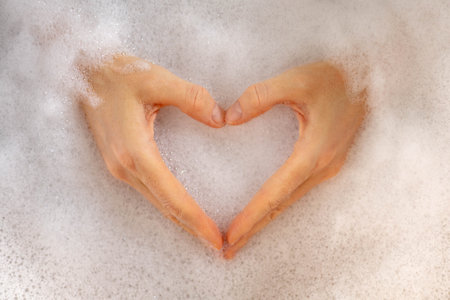 A heart made of female hands is filled with white foam and a bath. Concept of self-love, relaxationの写真素材