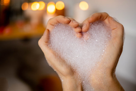 A heart made of female hands is filled with white foam and a bath. Concept of self-love, relaxationの写真素材