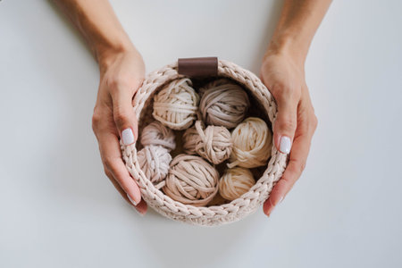 Female hands holding a crocheted basket with skeins of cotton yarn in natural tones and colors.の写真素材