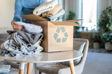 Female hands put clothes to recycling zero waste reusing cardboard box on table at home closeupの写真素材