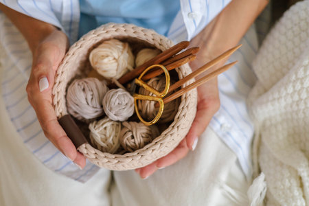 A woman in stylish clothes holds a crocheted basket with skeins of cotton yarn in natural tonesの写真素材