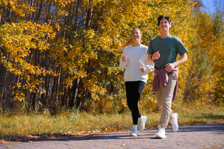 Sporty family couple morning jogging in city autumn beautiful park. Young active man, woman runnersの写真素材