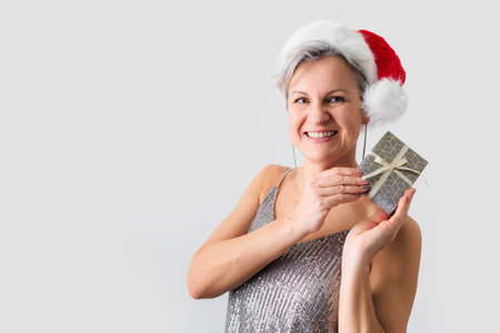Beautiful smiling middle-aged woman in Santa Claus hat holding gift in handsの写真素材