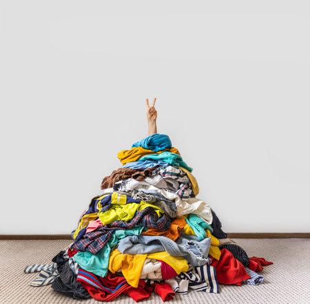 Unrecognizable human raises arm reaches out heap of colorful unfolded clothes busy doing wardrobe