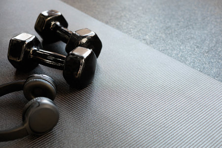 Headphones and black dumbbells lie on a black yoga mat. Flat lay. Space for text.の写真素材