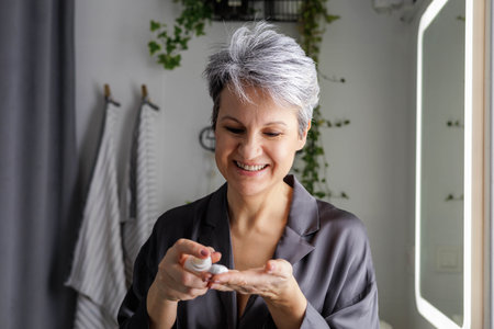 Mature beautiful woman during menopause with gray hair applies hormonal anti-aging creamの写真素材