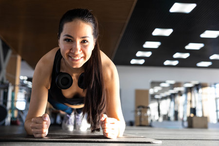 Smiling fitness woman stand in plank position doing push ups training at gym.