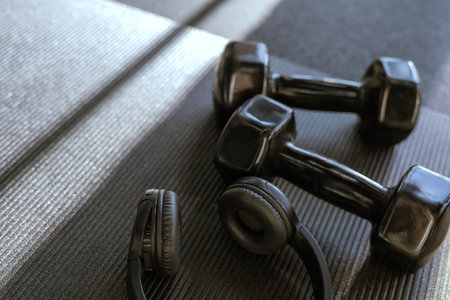 Black dumbbells for sports and headphones lie on the floor in the gym on a yoga matの写真素材