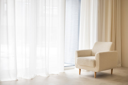 A white beautiful stylish chair stands near a large floor-to-ceiling window. Light curtains.の写真素材