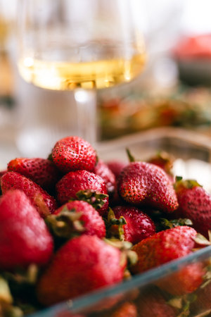 Fresh ripe strawberries in glass bowl with wine glass in soft focus background, summer fruit conceptの写真素材
