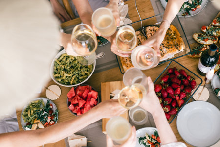 Group of friends toasting with wine over festive table with pasta, salmon, strawberries, watermelonの写真素材