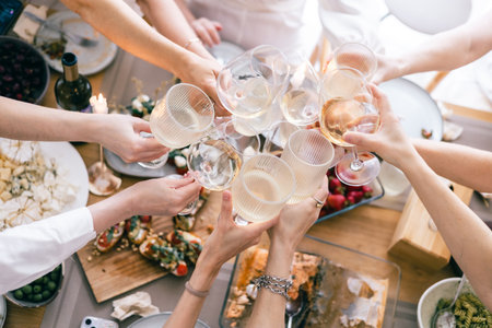 Top view of hands toasting with white wine over festive lunch table with cheese, bruschetta, pastaの写真素材
