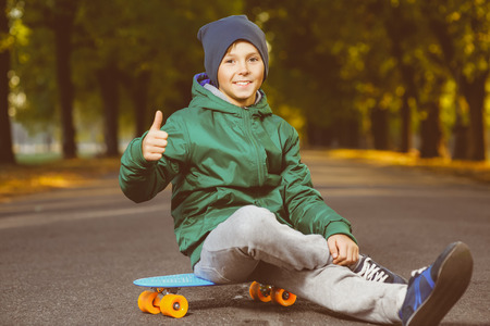 Smiling boy sitting on color plastic penny board or skateboards outdoor and showing thumbs up.の写真素材