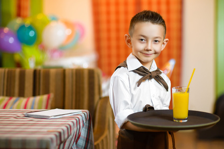 Happy cute little boy smiling waiter holding a tray width juice.の写真素材