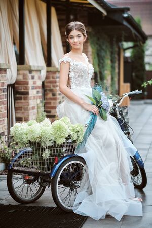 Gorgeous young bride outdoors with bike and basket full of flowersの写真素材