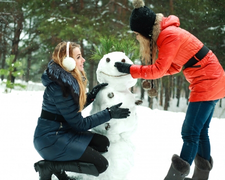 Two happy pretty girls building a snowman in pinewood on a winter dayの写真素材
