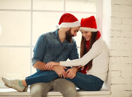 Happy young couple in red Christmas hats sitting on the windowの写真素材