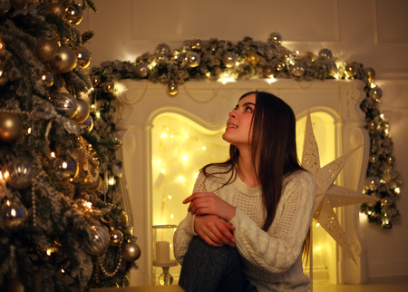 Dreamy young woman near a Christmas tree with lights decorating and presentsの写真素材