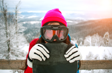 Portrait happy girl with a snowboard on top of a snowy mountainの写真素材