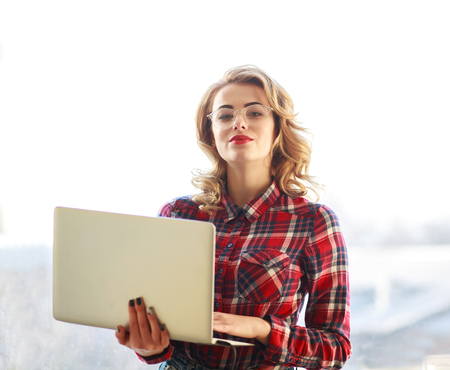 Attractive young woman in glasses stands with a laptop on whiteの写真素材