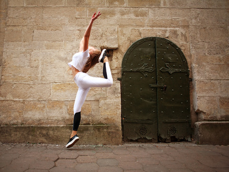 Sport athletic girl doing jumping exercises on the city street on background of vintage stone wallの写真素材